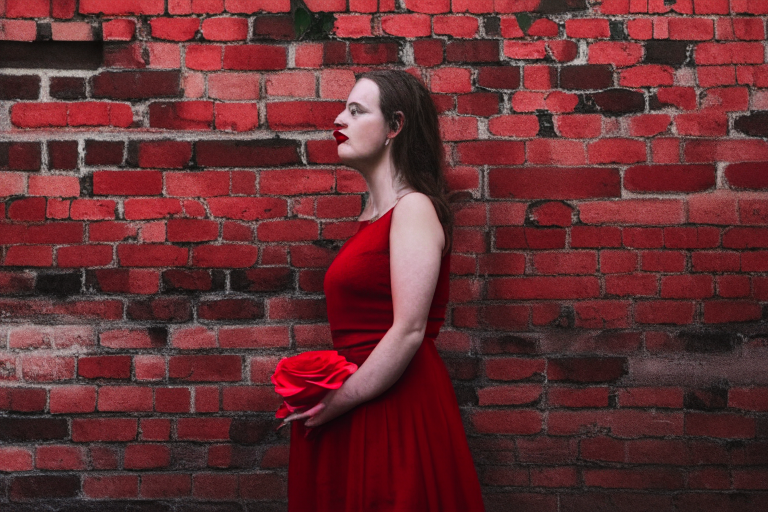 a woman wearing a red dress holding a rose, standing in front of a brick wall