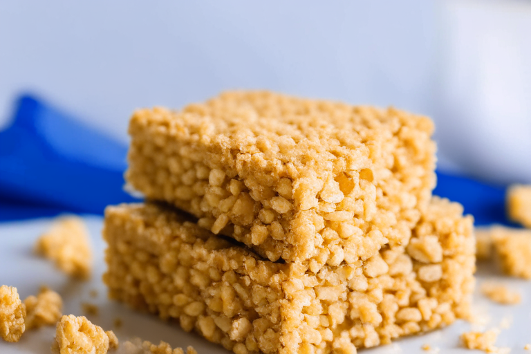 Gluten-free peanut butter rice krispie treats on a white plate, filling most of the frame under soft, directional studio lighting with razor-sharp focus on the entire treat