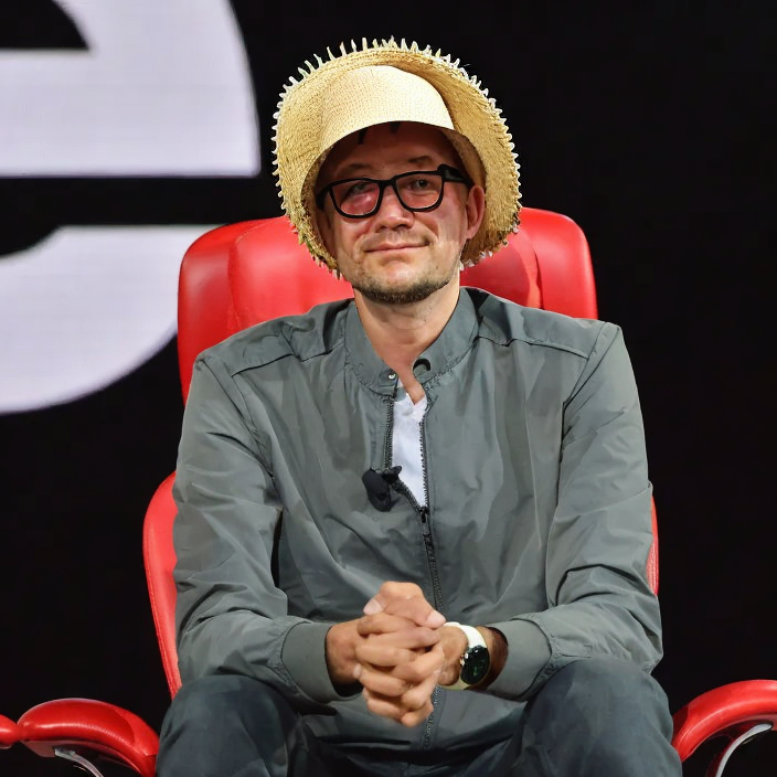 a man in glasses sitting in a red chair with a straw hat on his head