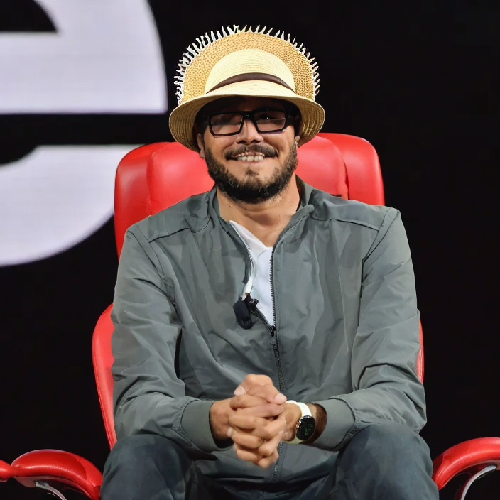 a man in glasses sitting in a red chair with a straw hat on his head