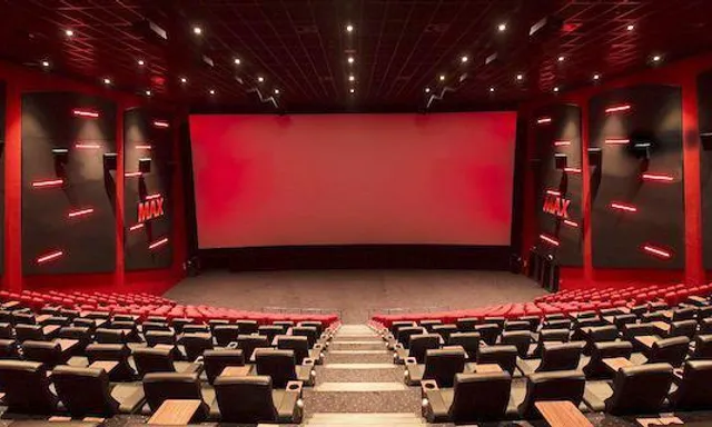 a large auditorium with rows of seats and a projector screen. chair, stage is empty, entertainment, textile, architecture, interior design, building, red, technology, hall