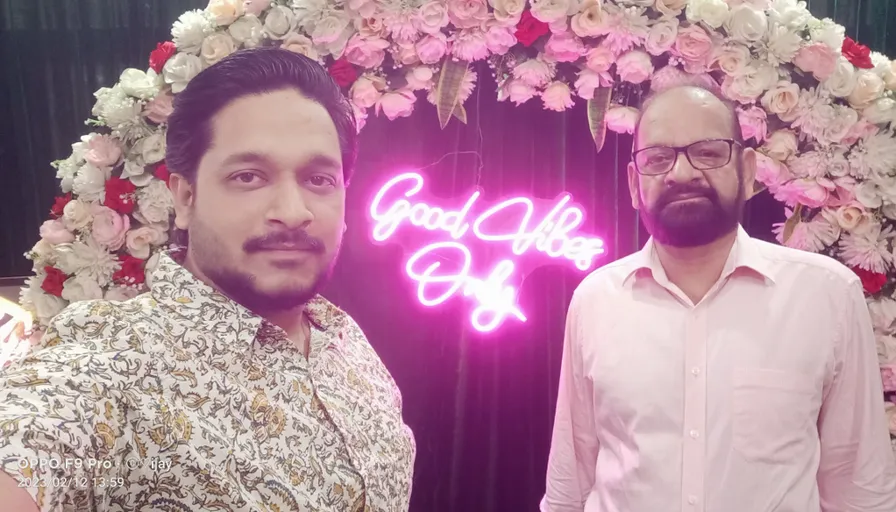 two men standing next to each other in front of a floral arch