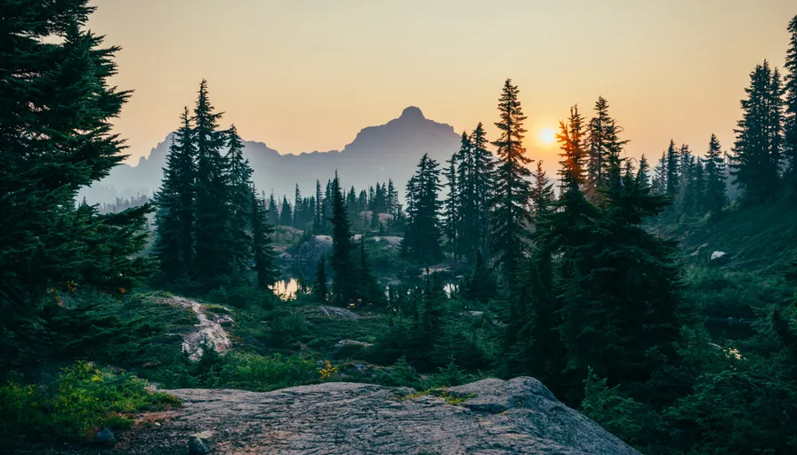 the sun is setting over the mountains and trees