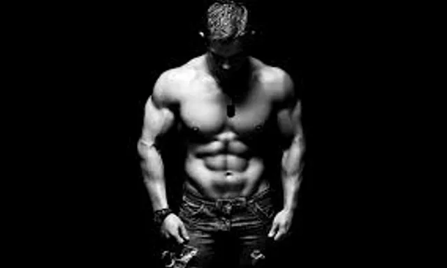 a shirtless man standing in the dark with his hands on his hips