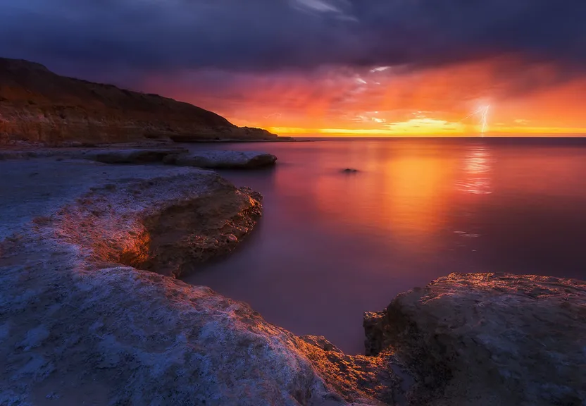 a sunset over a body of water with rocks in the foreground