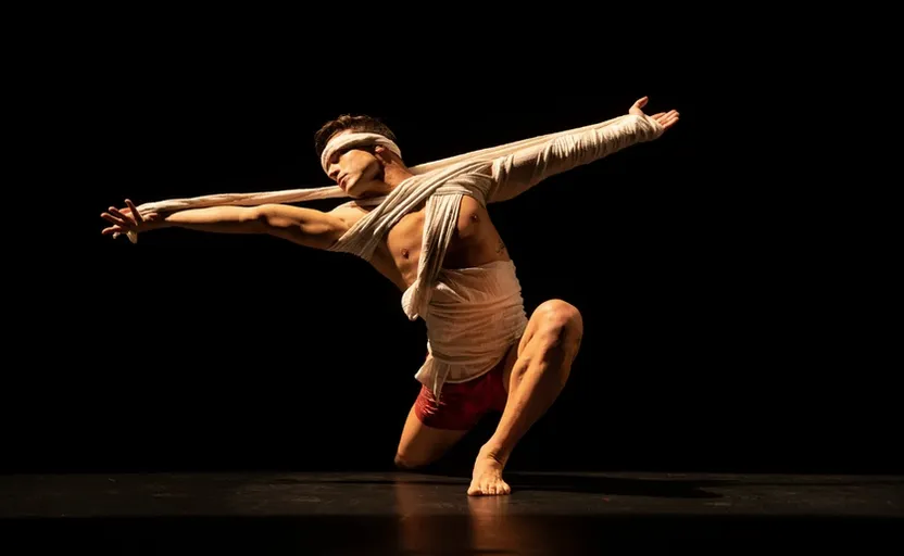 a male dancer with his arms outstretched on a dark stage