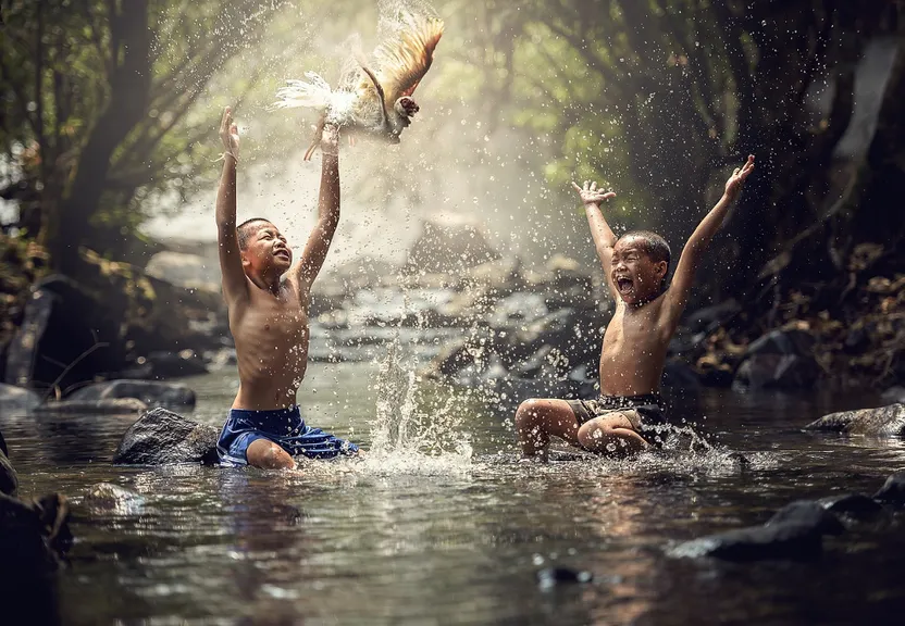 two young boys playing in a stream with a bird