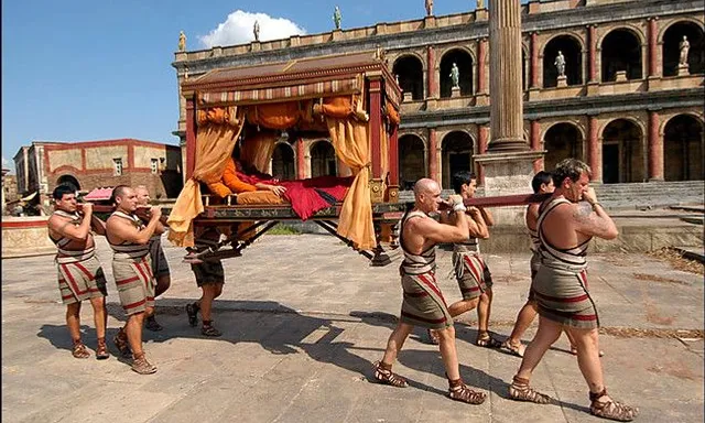 a group of men in roman garb carrying a bed