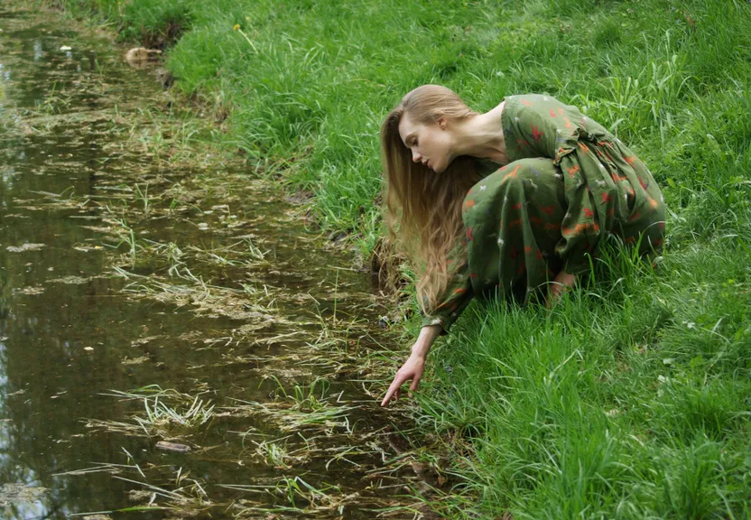 a woman kneeling down next to a body of water