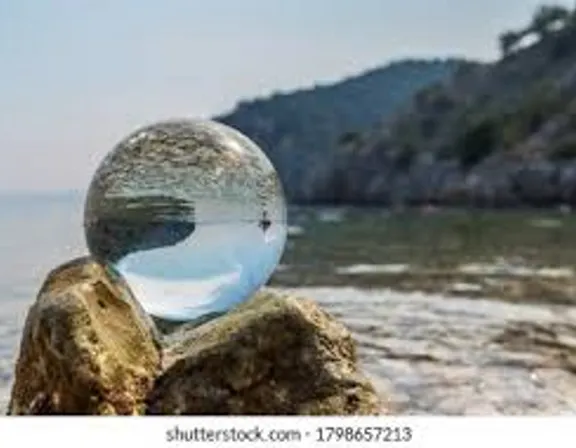 a glass ball sitting on top of a rock near the ocean