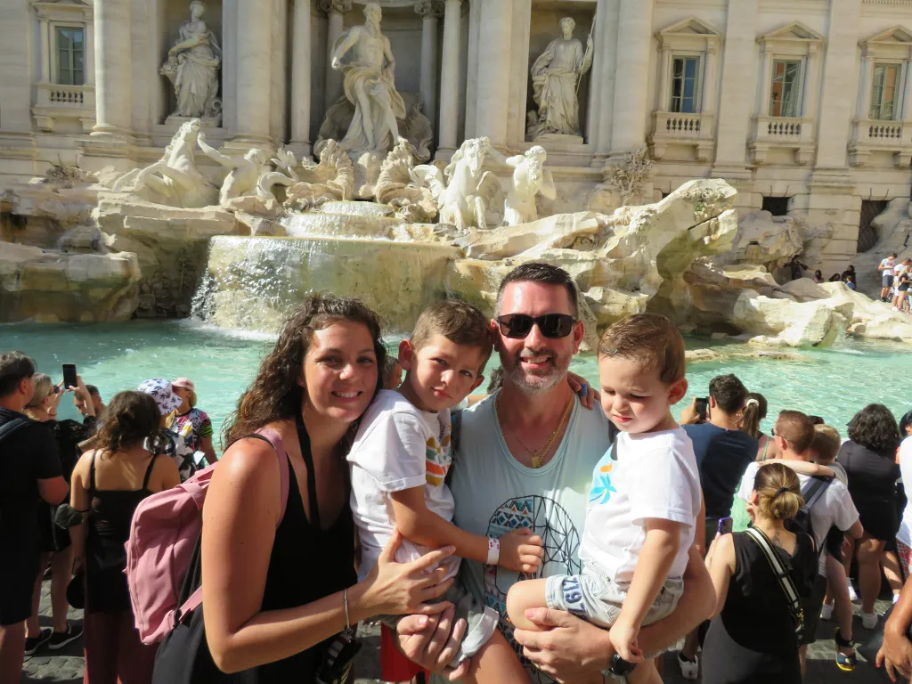 A photo of a man with two children by the Trevi Fountain in Rome. The water ripples and moves behind them.