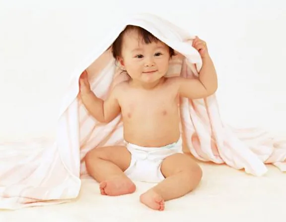 a baby is sitting under a blanket on the floor. face, skin, stomach, human body, flash photography, comfort, baby & toddler clothing, gesture, happy, pink