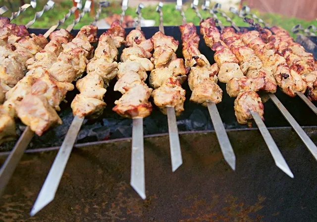 several skewers of meat are being cooked on a grill at a BBQ party. skewered meat is being served on a skewer on a grill