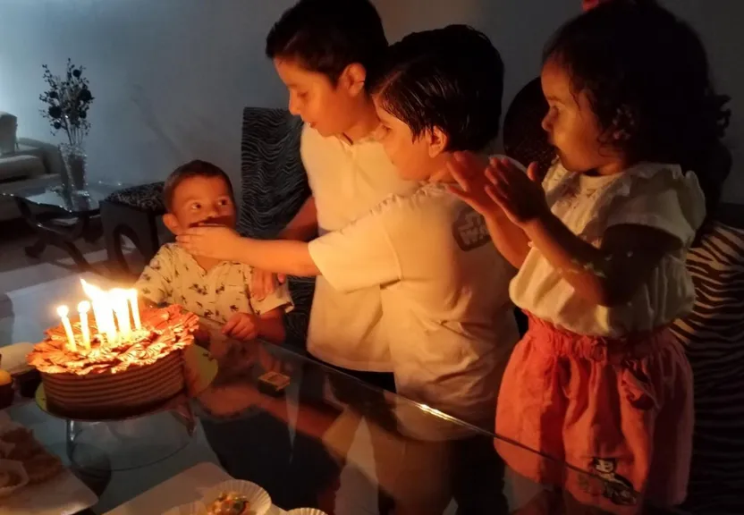 a group of people standing around a cake with lit candles