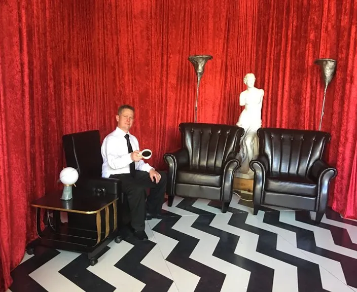 a man sitting in a chair in front of a red curtain