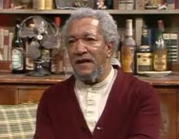 an old man sitting on a couch in front of a bookshelf