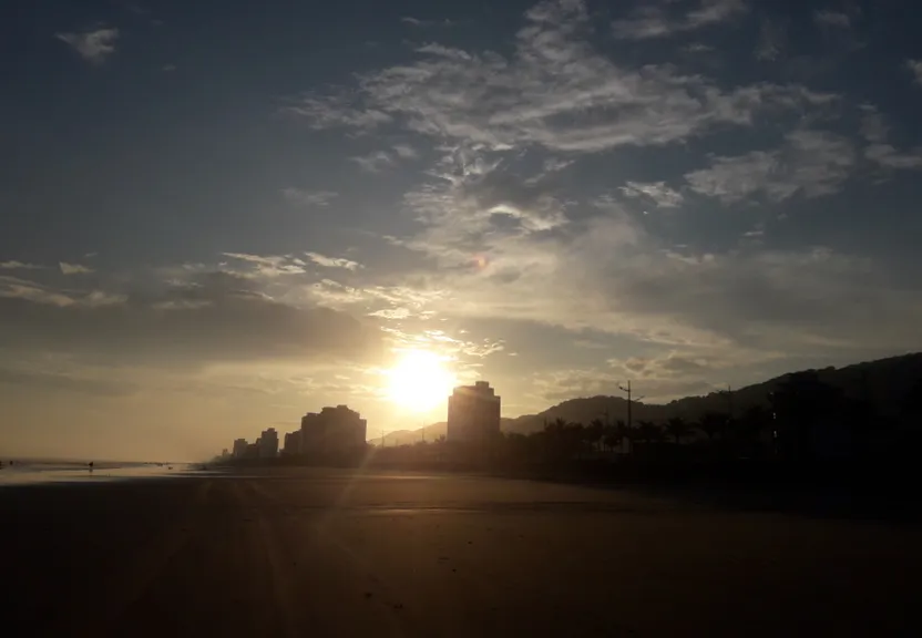 the sun is setting on the beach with buildings in the background