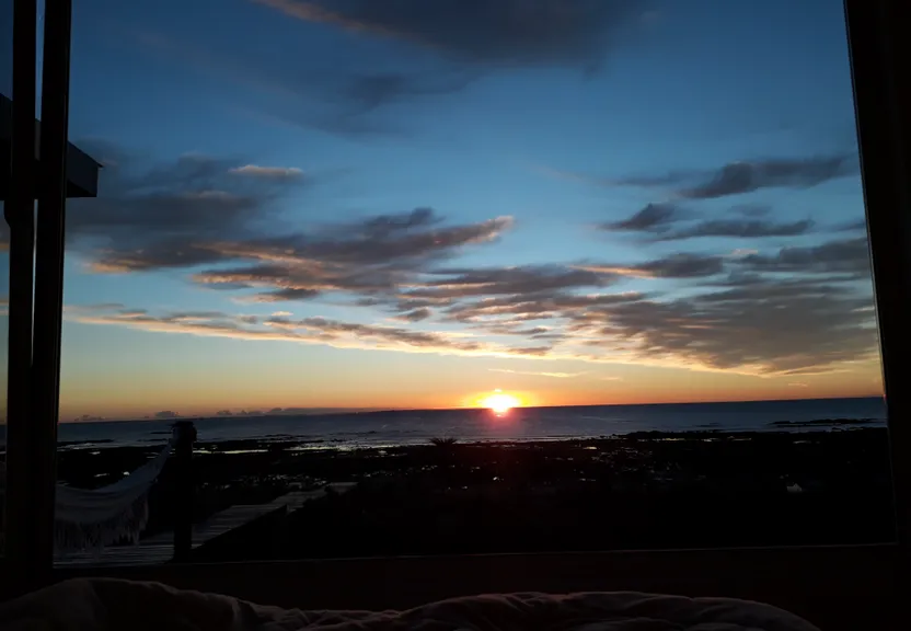 the sun is setting over the ocean from a bedroom window