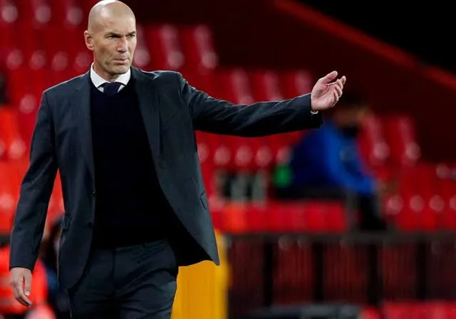 Zidane in a suit and tie is on the sidelines make him look like a real Zidane the footballer