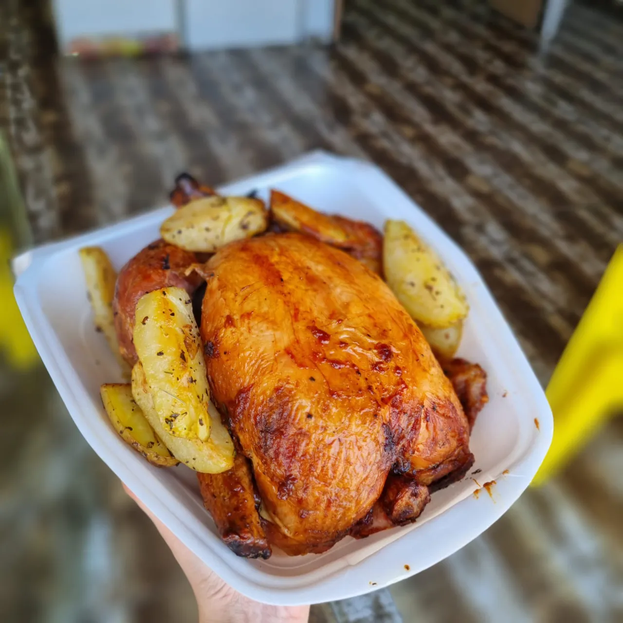 a person holding a plate of chicken and potatoes