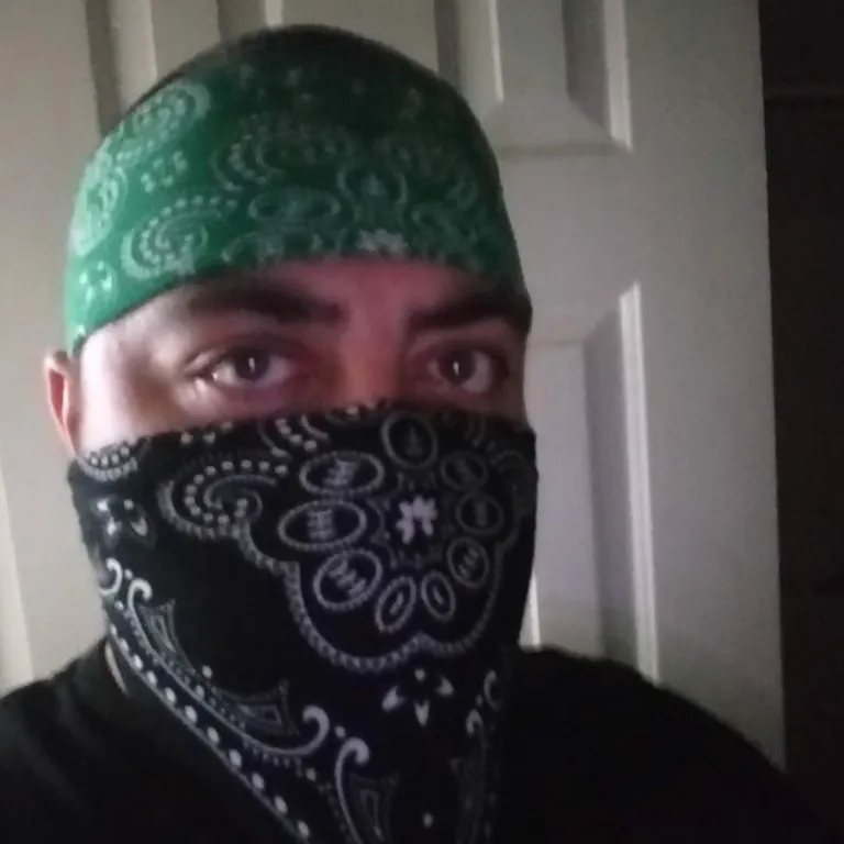 a man with a bandana covering his face. forehead, chin, outerwear, shirt, eyebrow, eye, mouth, beard, cap, neck