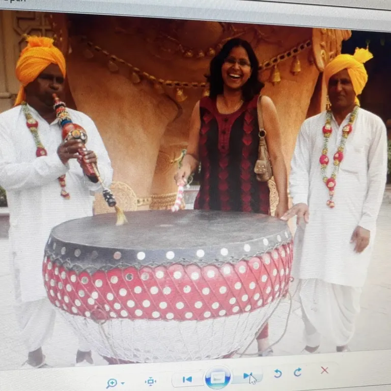 a group of people standing around a large drum. smile, table, human, fashion, hat, decoration, sunglasses, happy, beauty, event