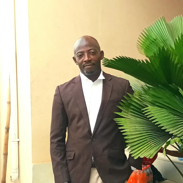 a man in a suit standing next to a potted plant