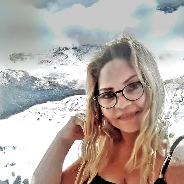 a woman wearing glasses standing in front of a mountain