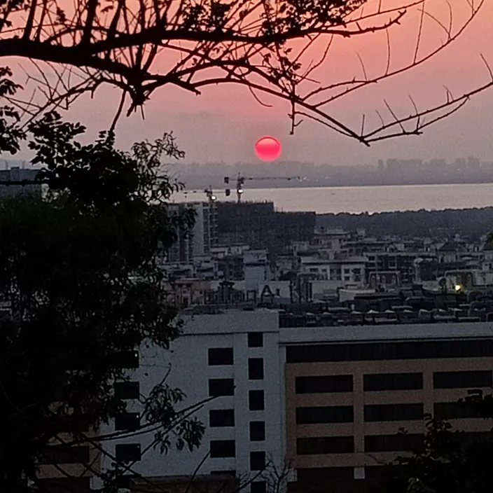 the sun is setting over a city with a body of water in the distance