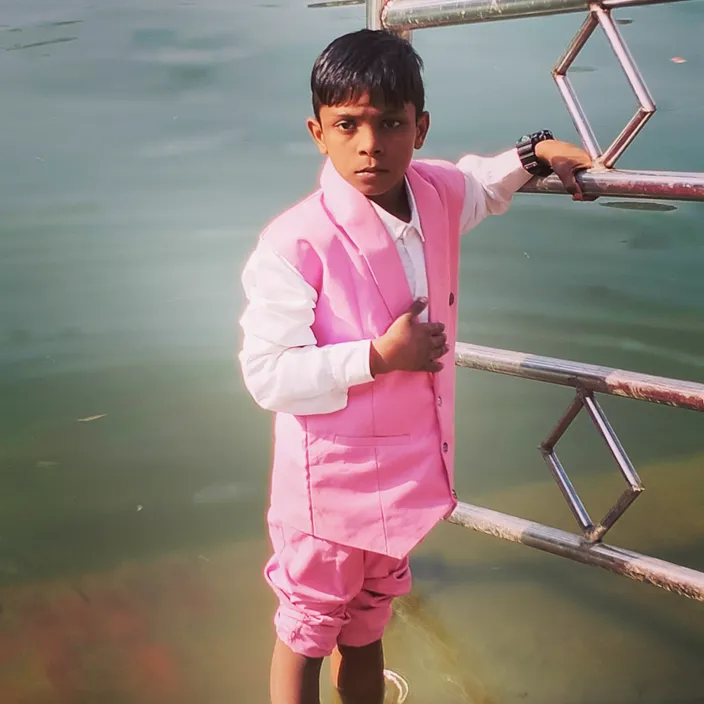 a young boy in a pink suit standing on a boat