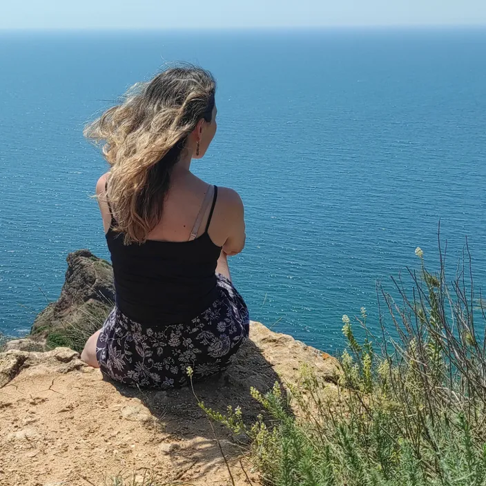 a woman sitting on a cliff overlooking the ocean