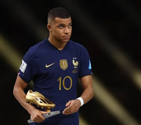 Kylian Mbappe holding a golden boot in his hands