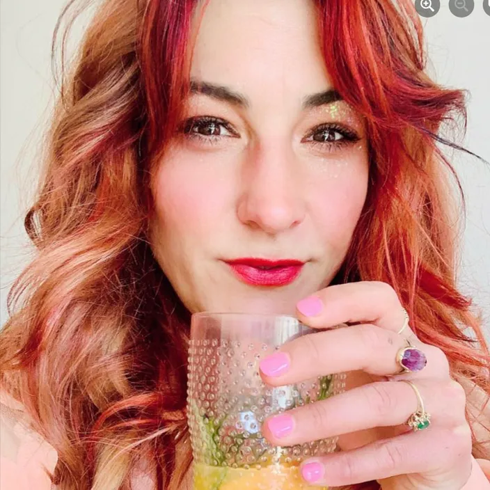 a woman with red hair holding a glass of liquid