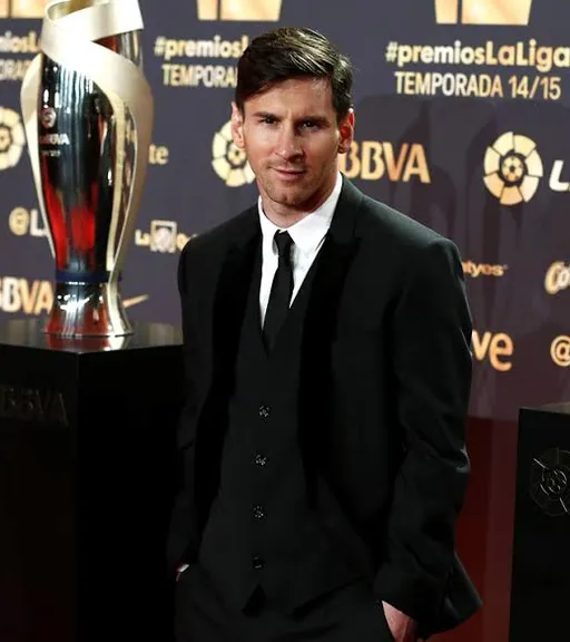 Messi in a suit standing next to a trophy