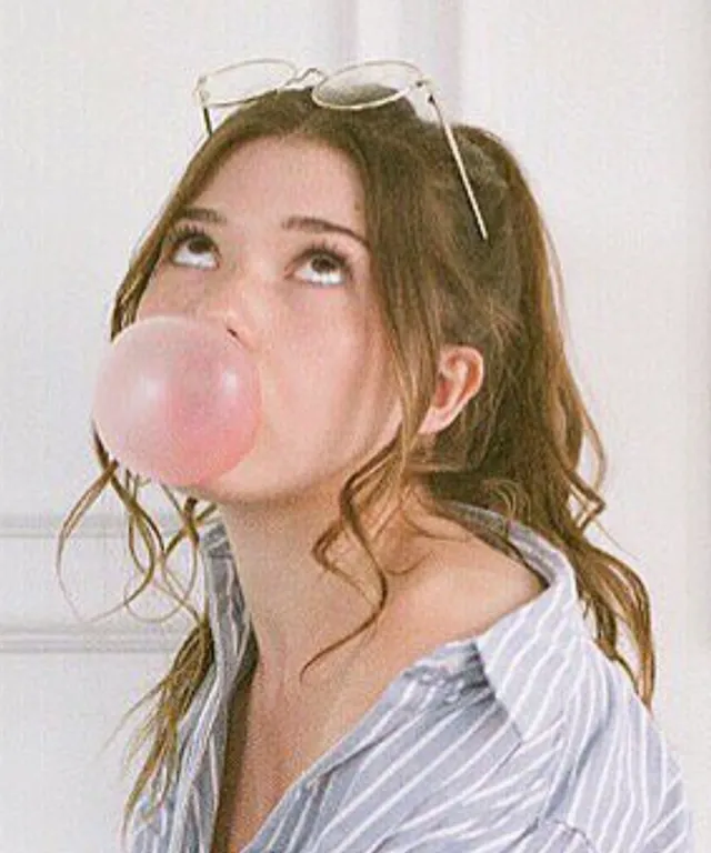 a woman blowing a bubble with a pair of glasses on her head