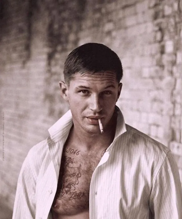 a man smoking a cigarette in front of a brick wall. tom hardy smoking a cigarette in front of a brick wall