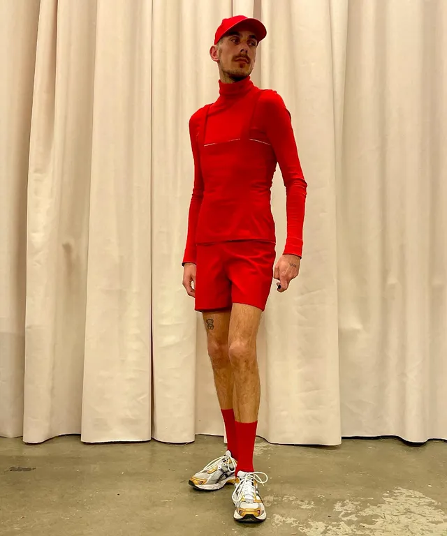 a man in a red outfit standing in front of a curtain