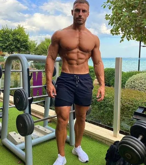 a man standing in front of a gym machine make him look like a real body builder