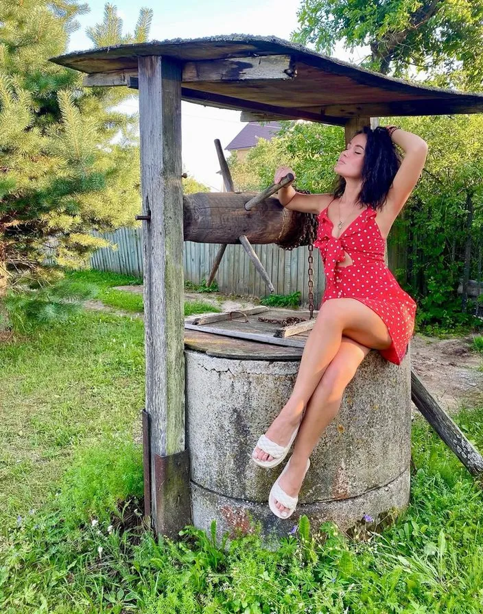 a woman in a red dress sitting on top of a water well