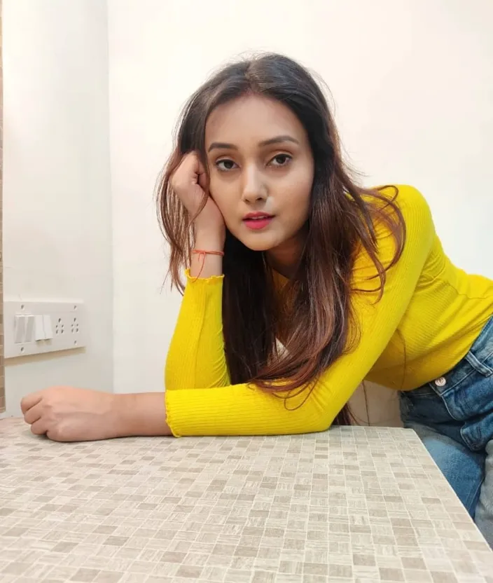 a woman sitting at a table with her hand on her head. clothing, facial expression, sleeve, waist, thigh, flash photography, flooring, floor, black hair, knee