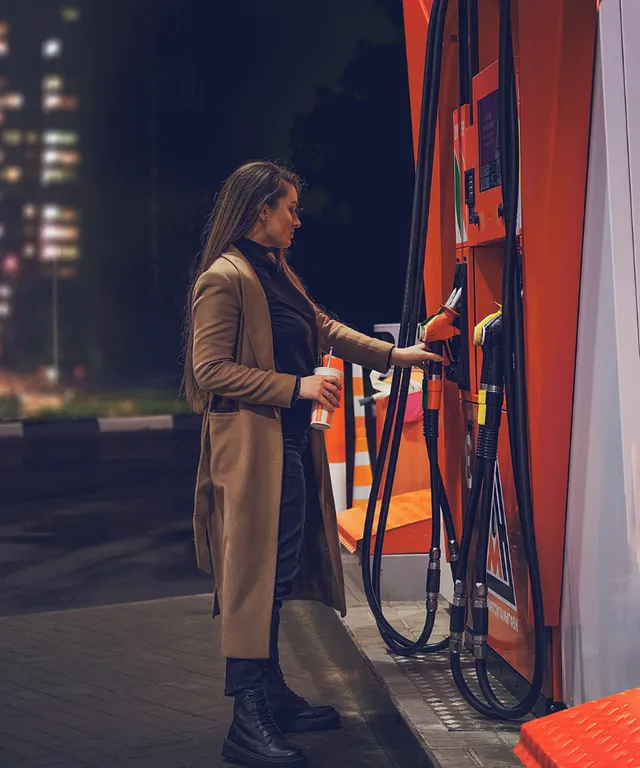 a woman filling up her car at a gas station at night