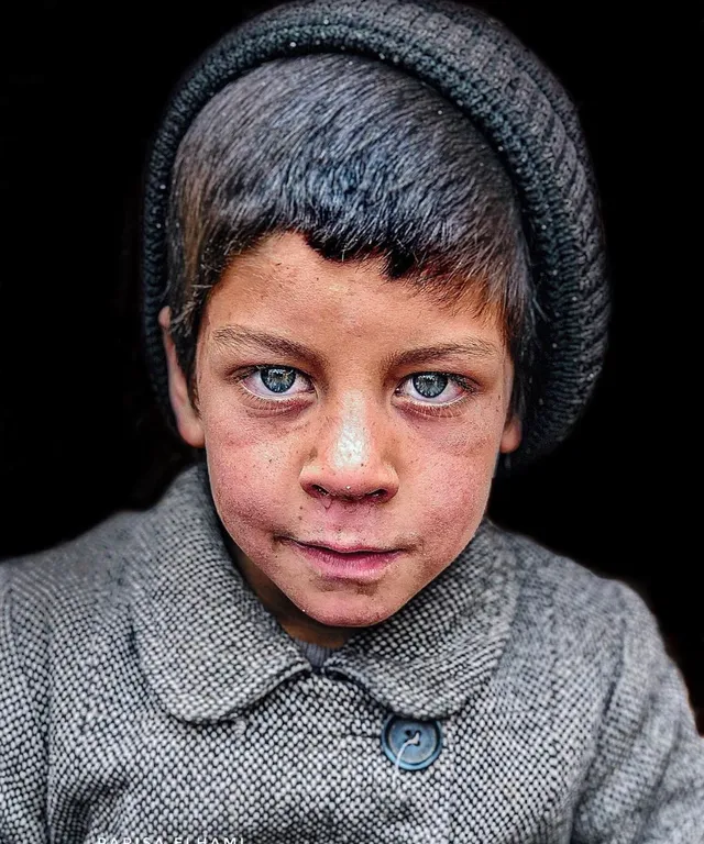 a young boy with blue eyes wearing a hat