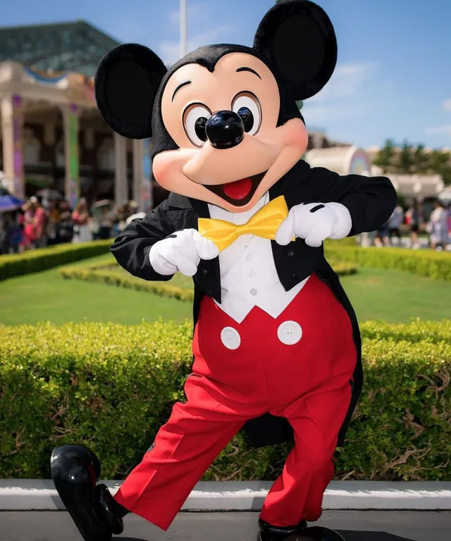 a person in a mickey mouse costume standing in front of a hedge