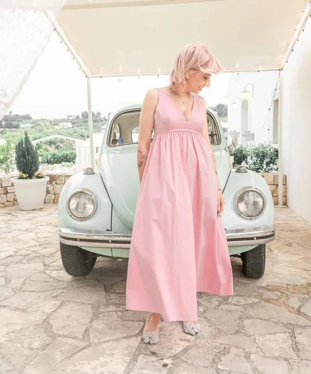 a woman in a pink dress standing next to a car