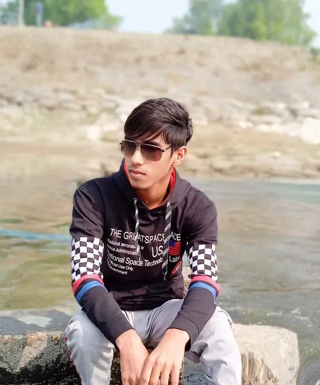 a young man sitting on a rock next to a river