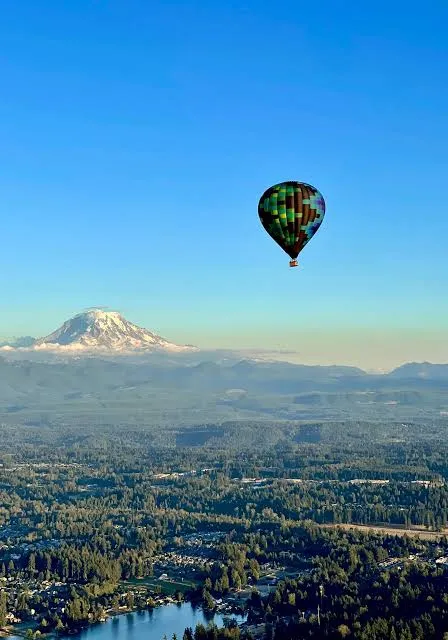 a hot air balloon flying over a lake and mountains