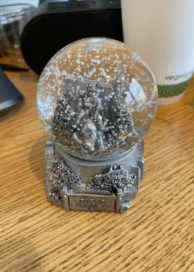 a snow globe sitting on top of a wooden table. liquid, wood, tableware, glitter, rectangle, metal, natural material, fashion accessory, hardwood, nail polish