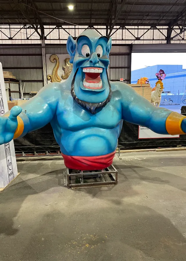 a large blue statue of a man on a cart. blue, cartoon, smile, mammal, gesture, leisure, fun, mascot, recreation, electric blue