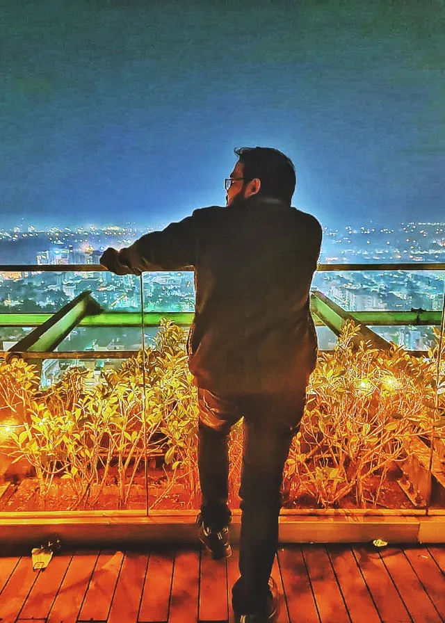 A Man Standing on a Wooden Floor Next to a Rafting Railing and Seeing the Construction of a New Huge Building in Front of Him. Big beautiful interesting building and getting constructed in front of him