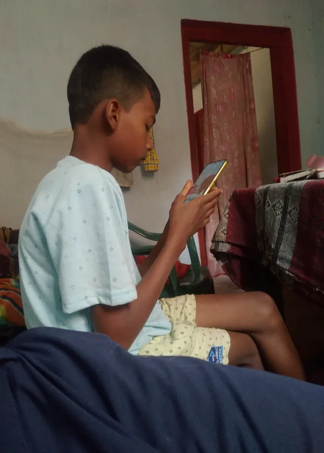 a young boy sitting on a bed looking at a book